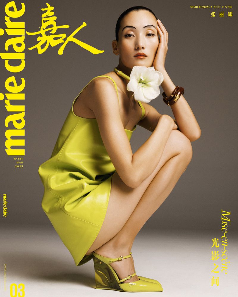 Marie Claire cover featuring a woman in a yellow dress and sculptural heels squatting against a grey background. White flower necklace.