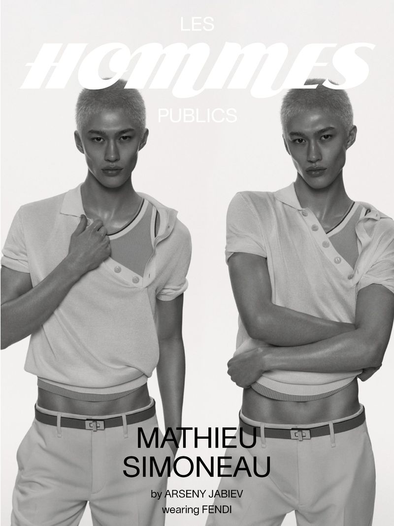 Two male models showcase fashion in a studio, one holding his shirt, both in light-colored attire against a bright backdrop.