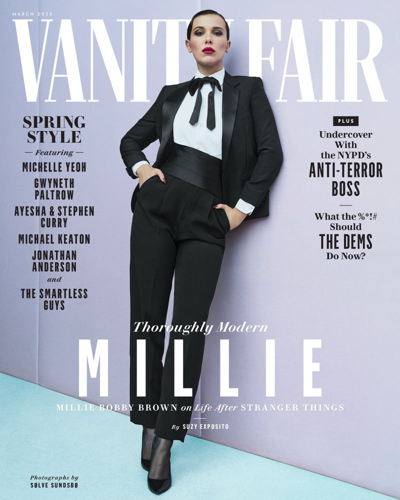 Magazine cover featuring Millie Bobby Brown in a black tuxedo with a bow tie, promoting a modern style, on a pale purple background.