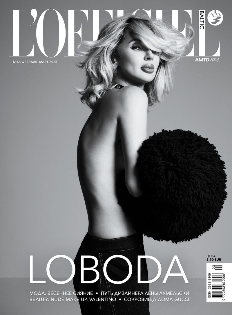 L'Officiel Baltic magazine cover featuring a bare-shouldered woman with blonde hair, jeans, and a black fluffy accessory against a gray background.