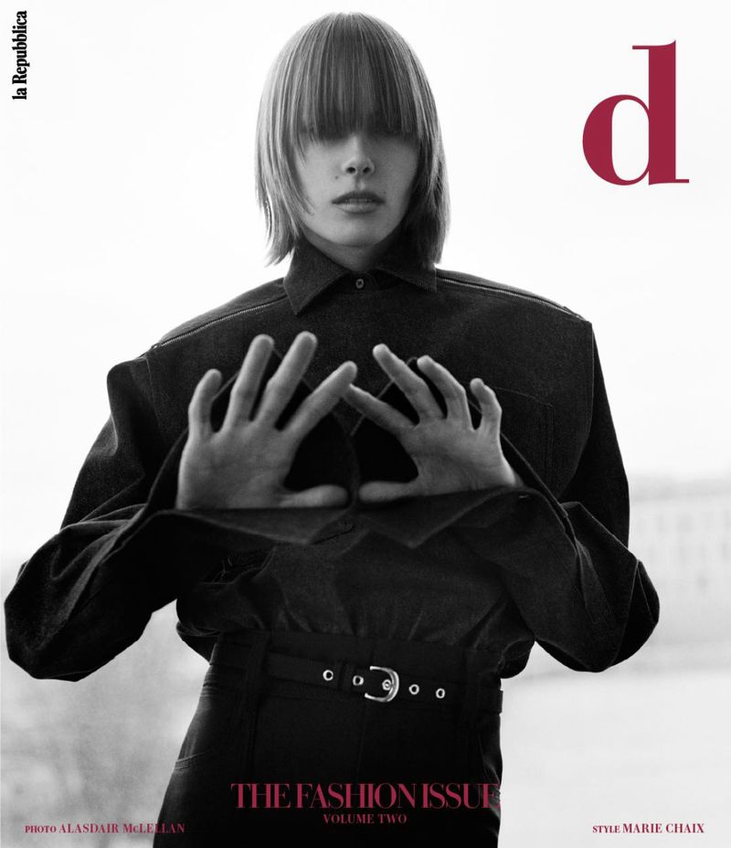 Editorial fashion shot features a person with blunt bangs, wearing a dark denim jacket and matching pants against a bright, diffused background.