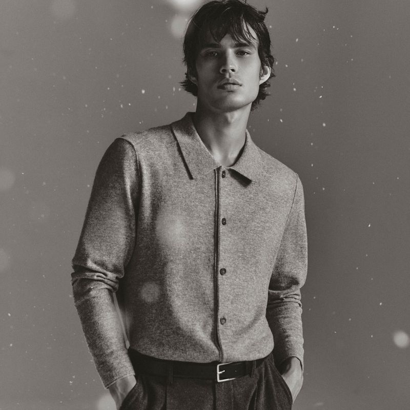 Monochrome portrait of a young man in a button-down shirt, posing indoors against a blurred background with bokeh lights, looking at the camera.