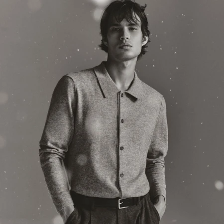 Monochrome portrait of a young man in a button-down shirt, posing indoors against a blurred background with bokeh lights, looking at the camera.