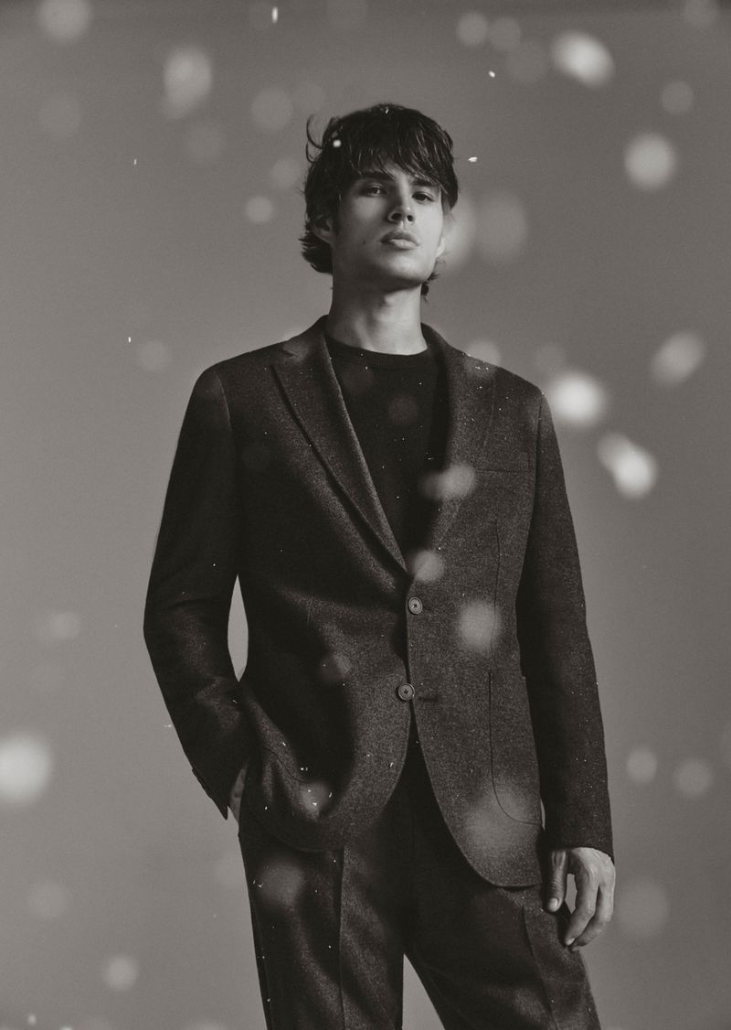 Monochrome portrait of a young adult male wearing a suit. He's looking upwards with an earnest expression in a studio setting.