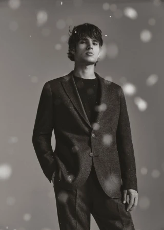 Monochrome portrait of a young adult male wearing a suit. He's looking upwards with an earnest expression in a studio setting.