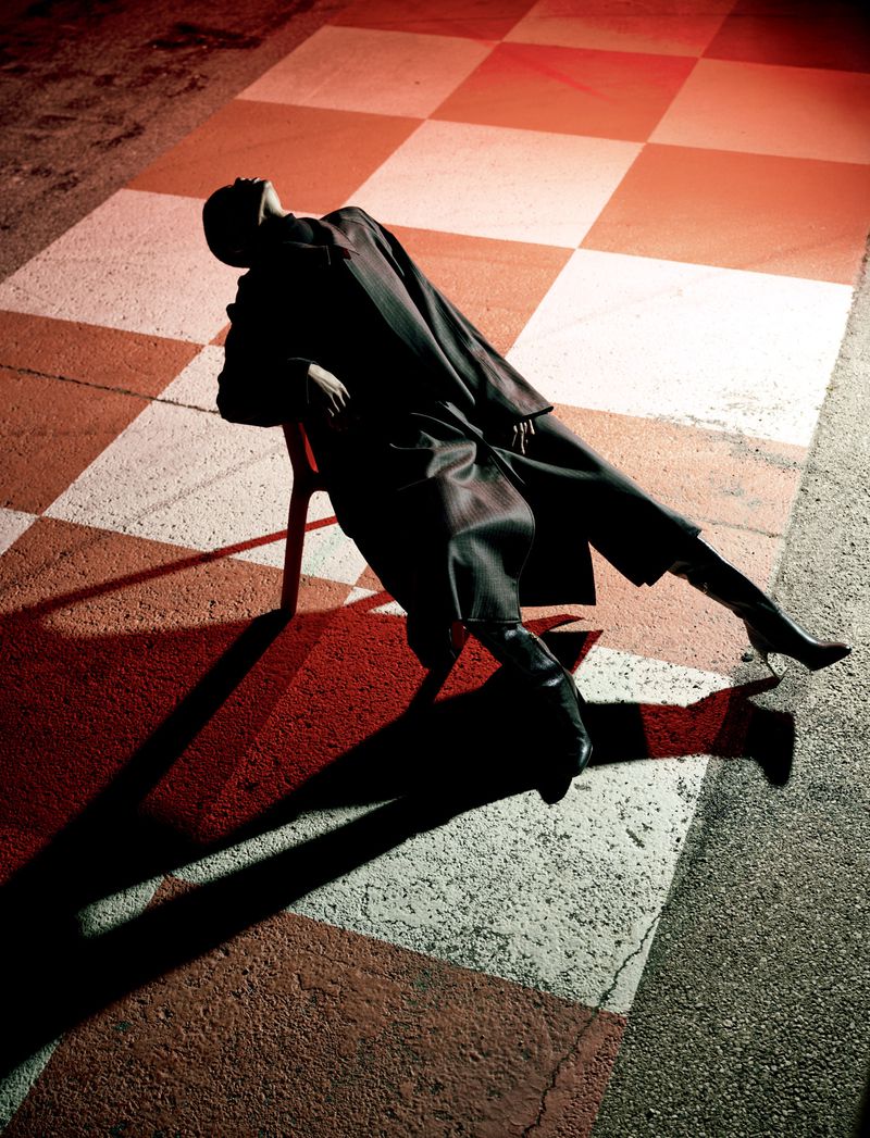 Stylish adult female lying on a chair on a checkerboard pattern in a dark scene, showcasing dark colours and high heels.
