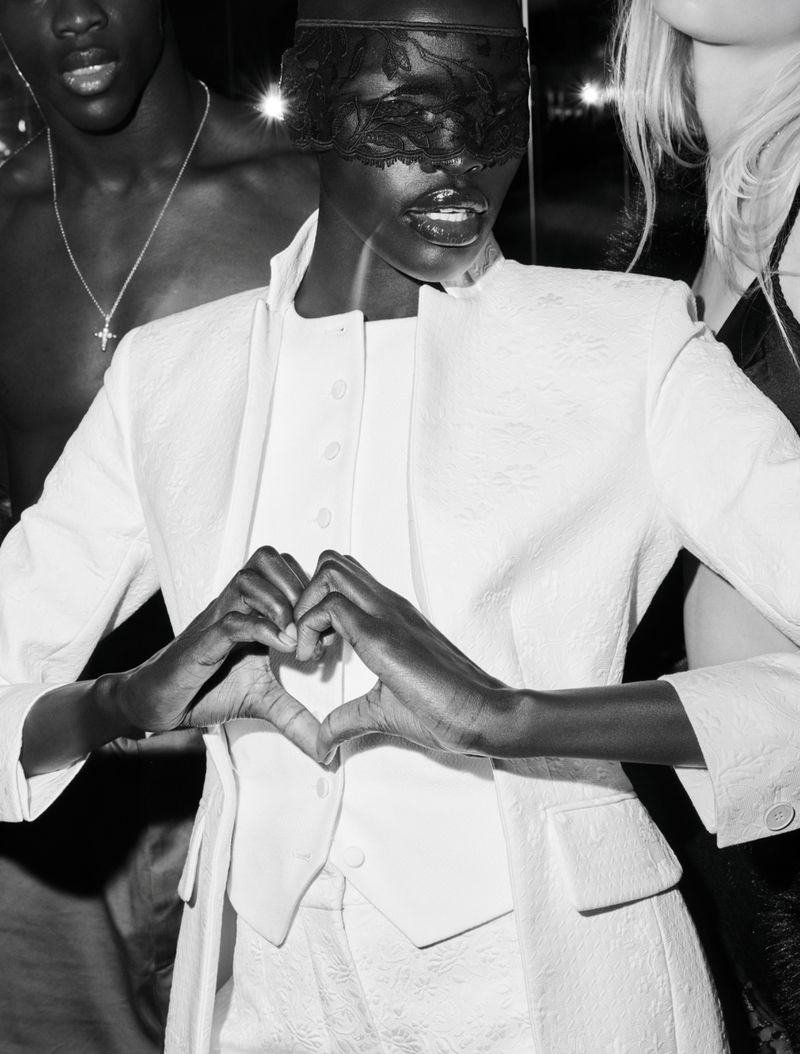 Three people pose in a black-and-white fashion shot. An African-American woman is wearing white clothing and a lace mask.