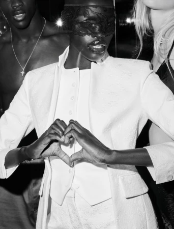 Three people pose in a black-and-white fashion shot. An African-American woman is wearing white clothing and a lace mask.