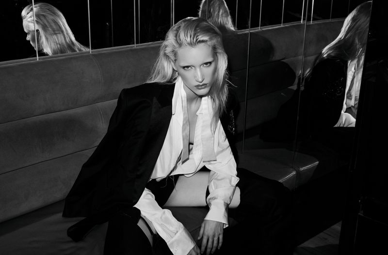 Black and white portrait of a blonde adult woman in a white blouse and dark jacket sitting on a couch in an indoor setting.
