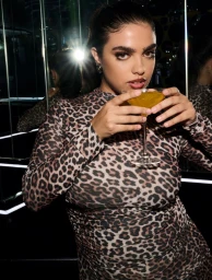 Model wearing a leopard print dress holding a cocktail in a nightclub setting for Vogue Greece