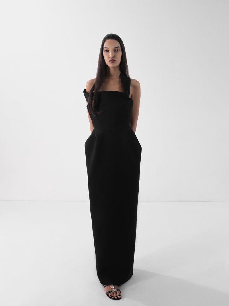 Elegant woman in black formal gown poses in a bright studio, showcasing fashion and style against a plain white backdrop.
