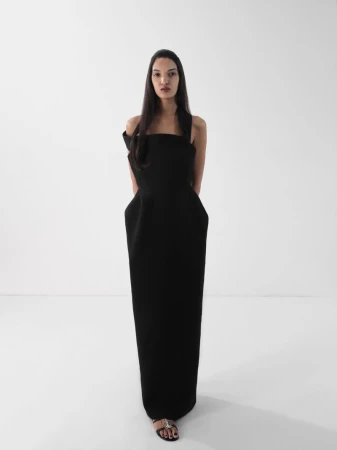 Elegant woman in black formal gown poses in a bright studio, showcasing fashion and style against a plain white backdrop.