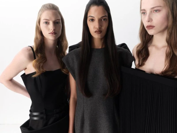 Three women in fashionable dresses in a studio, striking elegant poses, showcasing minimalist style, with fair and warm skin tones.