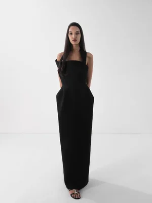 Model wearing a structured black evening dress against a bright white seamless studio background.