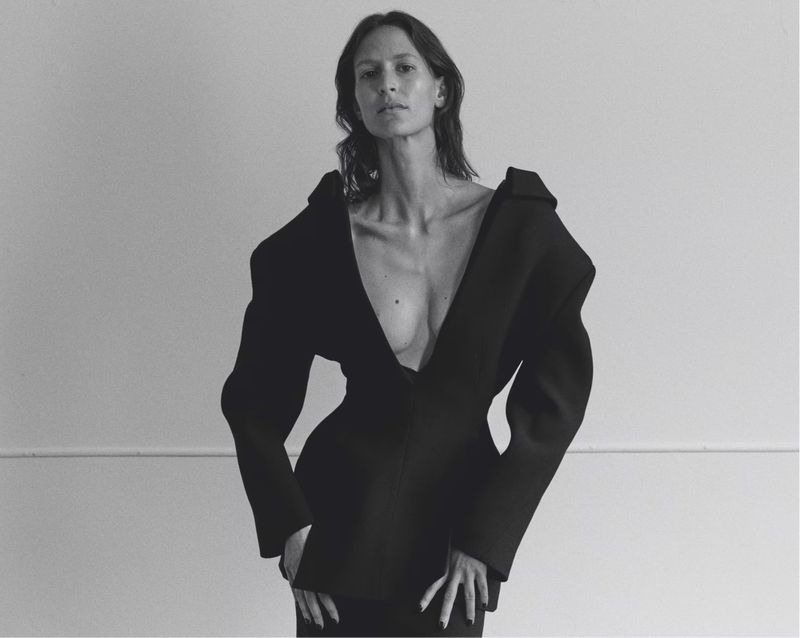 Model Jeanne Cadieu wearing an avant-garde black structural blazer with exaggerated shoulders against a studio wall.