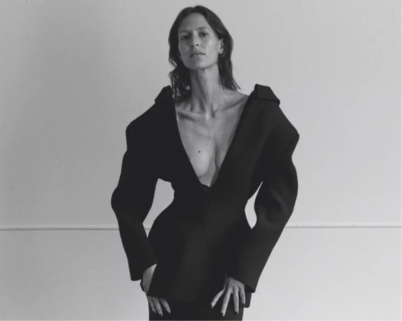 Model Jeanne Cadieu wearing an avant-garde black structural blazer with exaggerated shoulders against a studio wall.