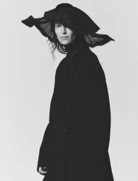Jeanne Cadieu wearing a wide-brimmed black hat and dark coat against a white background by Mel Bles.
