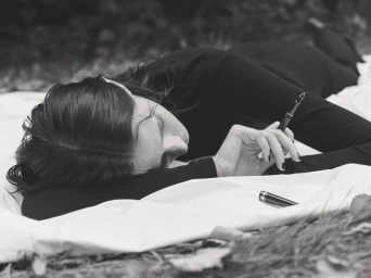 Jeanne Cadieu lying on white fabric holding a fountain pen in an editorial by Mel Bles for Ladybird