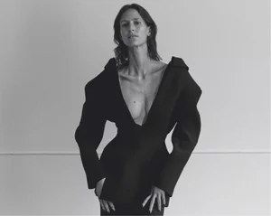 Model Jeanne Cadieu wearing an avant-garde black structural blazer with exaggerated shoulders against a studio wall.