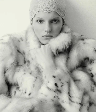 Model Lainey Hearn wearing an oversized spotted fur coat and lace cap in a black and white editorial portrait.