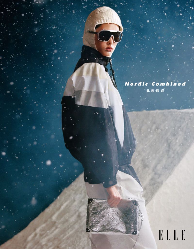 Fashionable woman in ski attire poses with a silver handbag against a snowy backdrop. Nordic Combined text and the ELLE logo are visible.