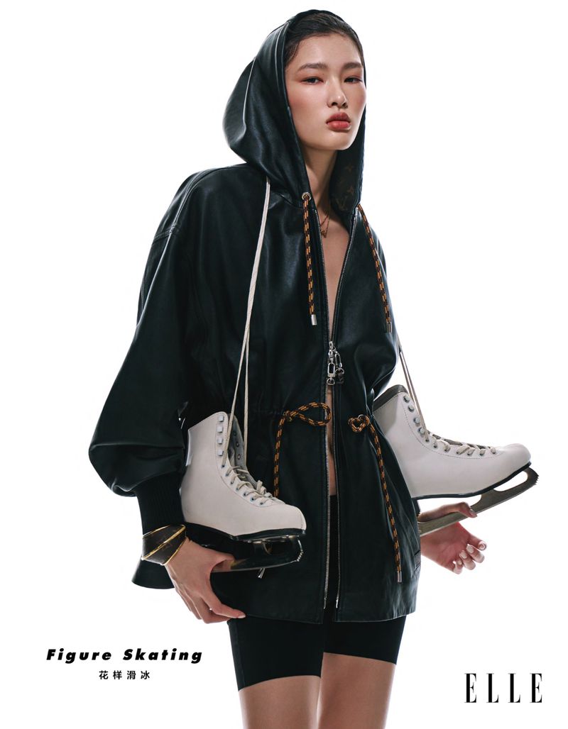 Stylish young woman poses with ice skates in a studio. She wears a hooded jacket and shorts. ELLE logo visible. 