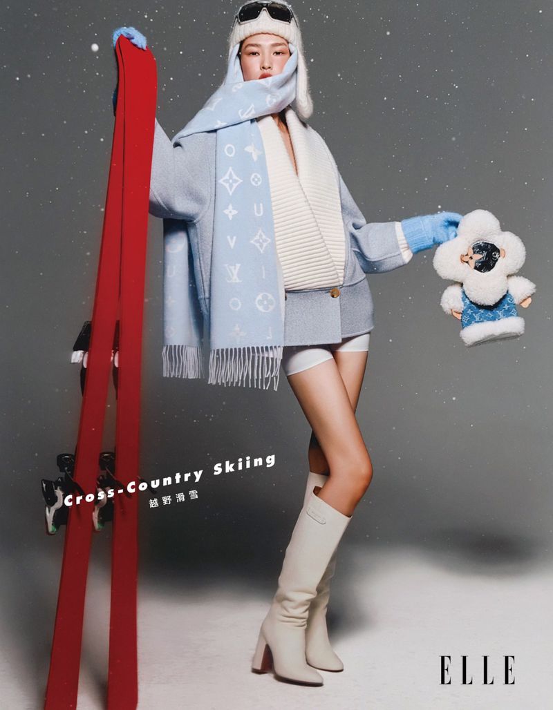 Asian woman in winter fashion poses with ski equipment and plush toy in a studio setting with a cool-toned color palette.