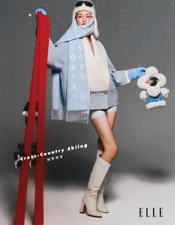 Asian woman in winter fashion poses with ski equipment and plush toy in a studio setting with a cool-toned color palette.