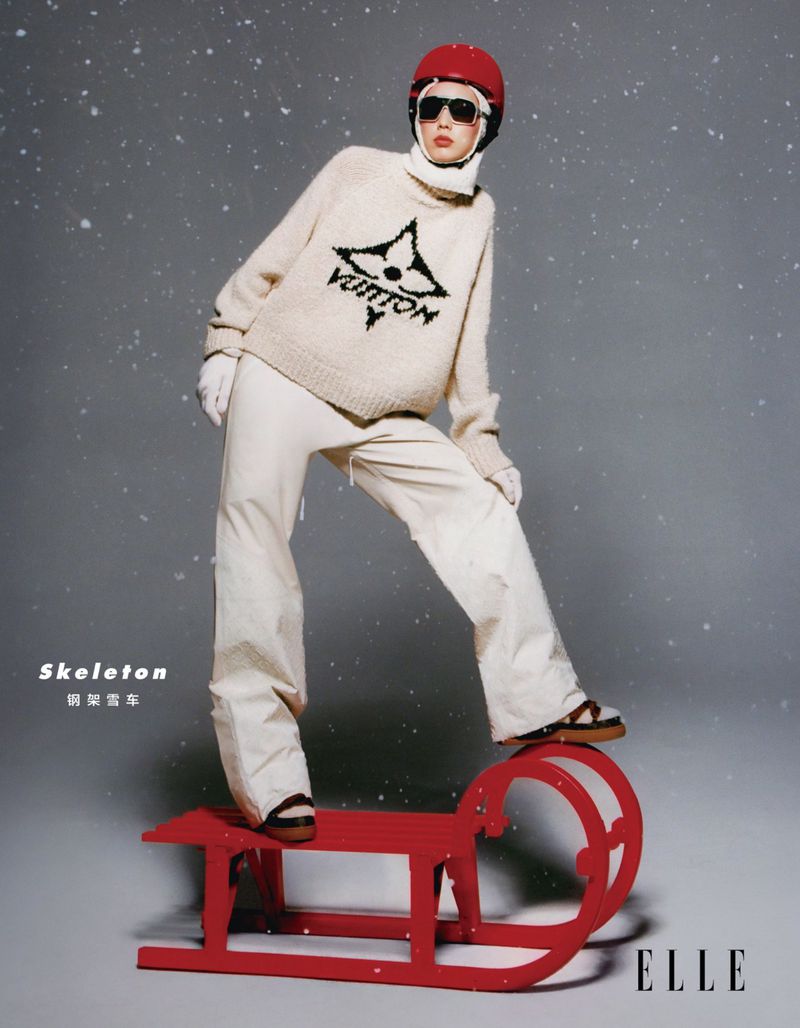 Fashion shot of a woman wearing a red helmet and an oversized sweater posing with a red sled in a studio with snow effect.