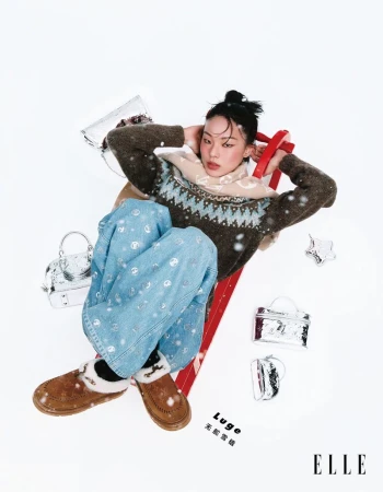 A young woman lies on a red sled surrounded by silver handbags and wearing wintery clothes in a studio fashion editorial.