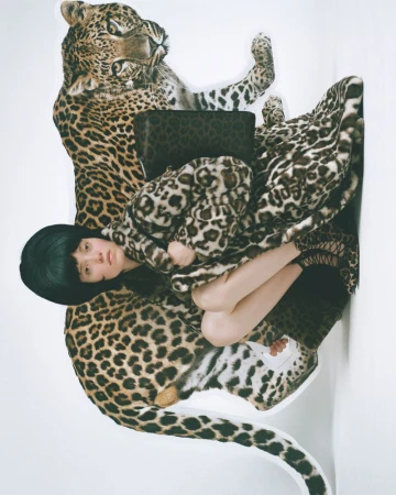 Fashion shot of a woman lying on a large faux leopard with matching leopard patterned clothing, on a white seamless background.