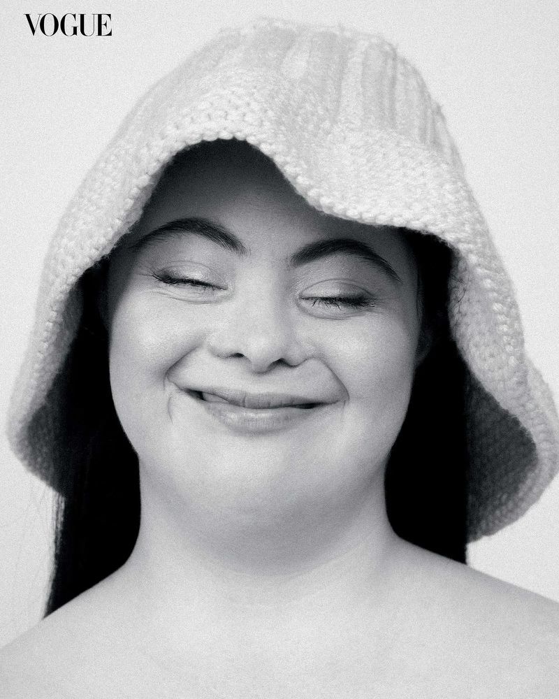 Monochrome portrait of a smiling adult woman wearing a knitted bonnet and dark hair against a plain white backdrop in studio light.