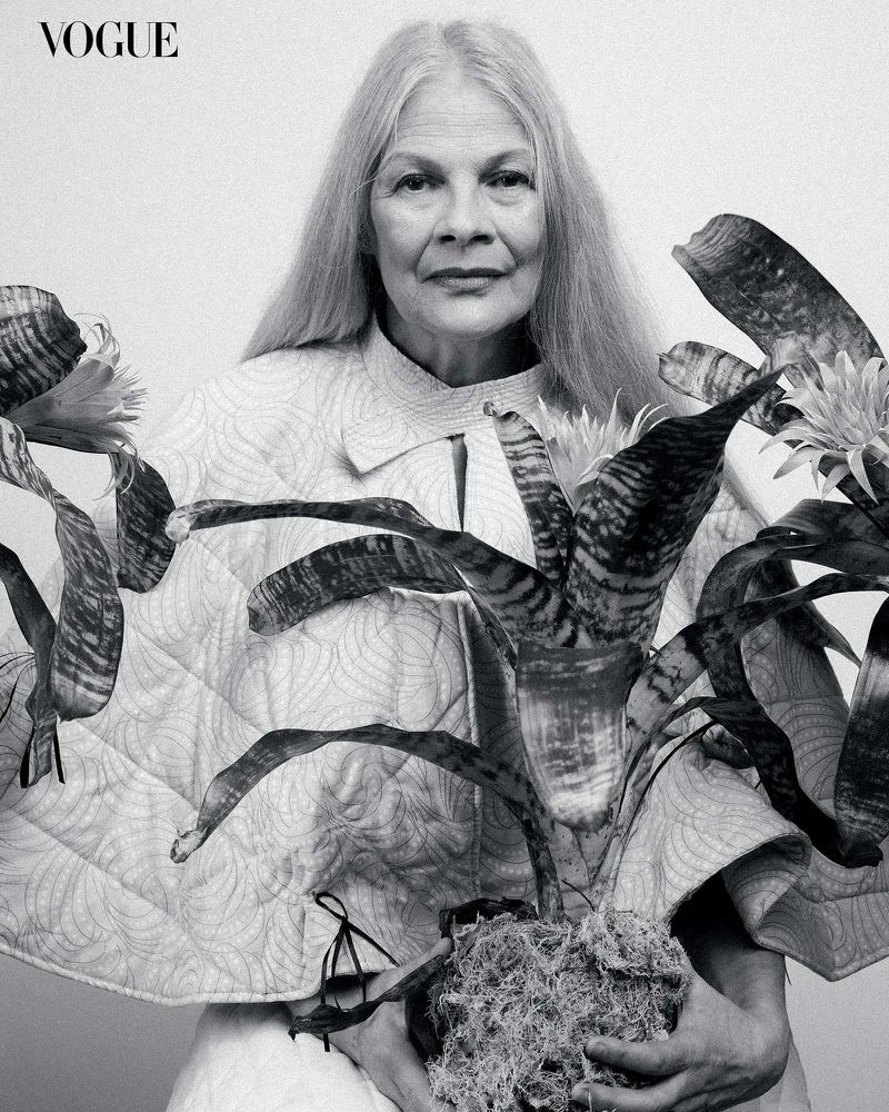 Black and white portrait of an elderly woman holding a potted plant against a white background in front of the Vogue logo.