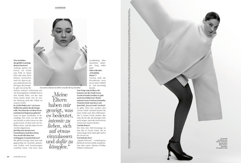 Editorial fashion shot of a woman in a white oversized sweatshirt, sheer tights, and black heels, posed against a bright white background.