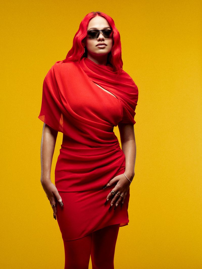 Adult female in red dress and matching sheer scarf and leggings poses against a bright yellow seamless backdrop wearing sunglasses.