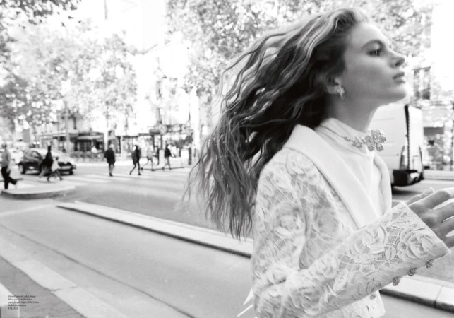 Black and white fashion portrait of a woman with long wavy hair walking on a city street, wearing a lace jacket.