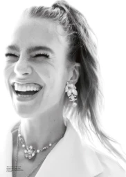 Black and white portrait of a laughing woman wearing crystal statement earrings and necklace against a bright white background.
