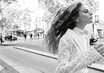 Black and white fashion portrait of a woman with long wavy hair walking on a city street, wearing a lace jacket.