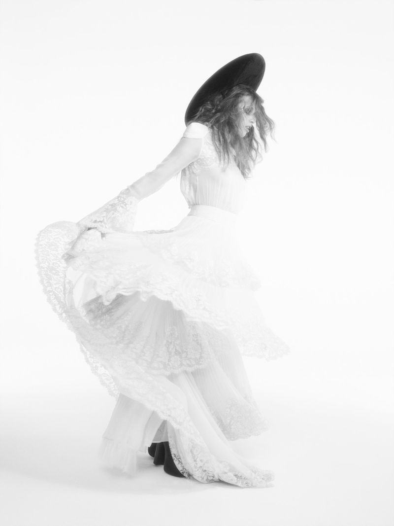Elegant woman in a white dress and black hat gracefully spins in a photo studio, showcasing fine art photography with a focus on fashion.