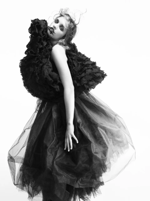 Black and white fashion portrait of a woman in a dramatic ruffled and tulle dress against a white background in a photo studio.