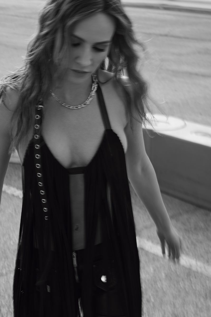Woman in a black halter top and pants stands outside in a monochrome portrait, wearing a chain necklace.