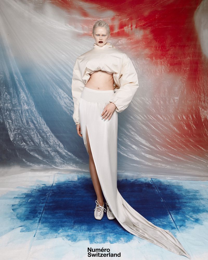 Fashion editorial image of a young adult woman with platinum hair wearing a white outfit with sneakers in a studio environment.