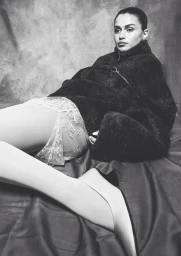 Monochrome fashion editorial image of Luisinha Oliveira wearing a dark fuzzy coat and lace briefs against a mottled backdrop.