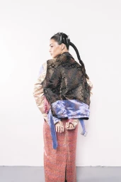 Model with dark hair in a long patterned skirt and jacket against a white background for Neo 2 magazine.