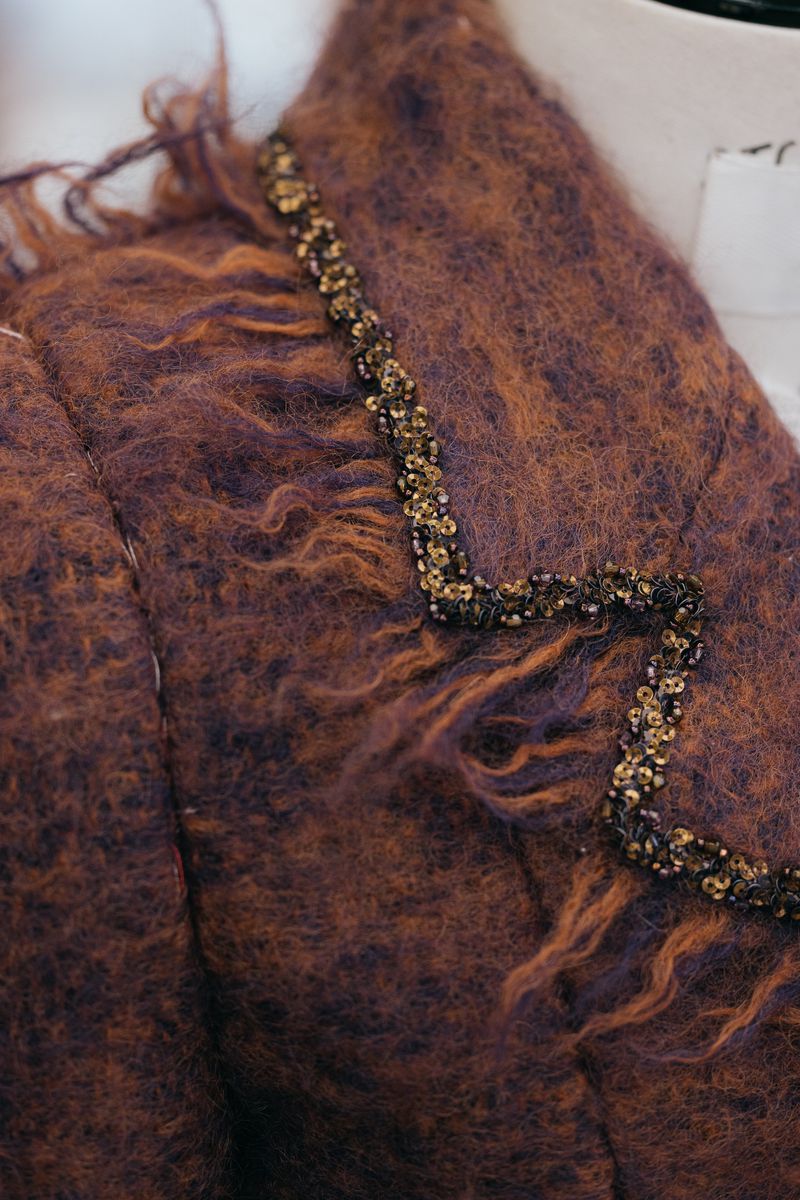 Close-up of a textured brown and purple mohair jacket with an embellished collar detail on a mannequin in a photo studio.