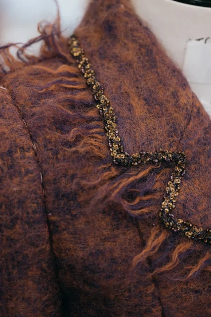 Close-up of a textured brown and purple mohair jacket with an embellished collar detail on a mannequin in a photo studio.