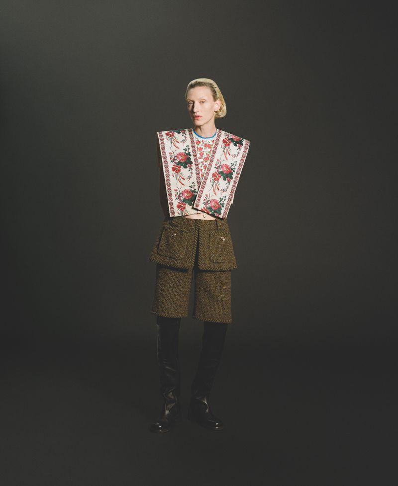 Adult female fashion model in floral top and textured shorts poses in a studio with a dark backdrop and dramatic lighting.