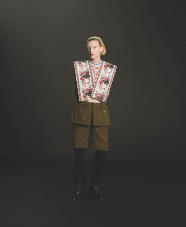 Adult female fashion model in floral top and textured shorts poses in a studio with a dark backdrop and dramatic lighting.