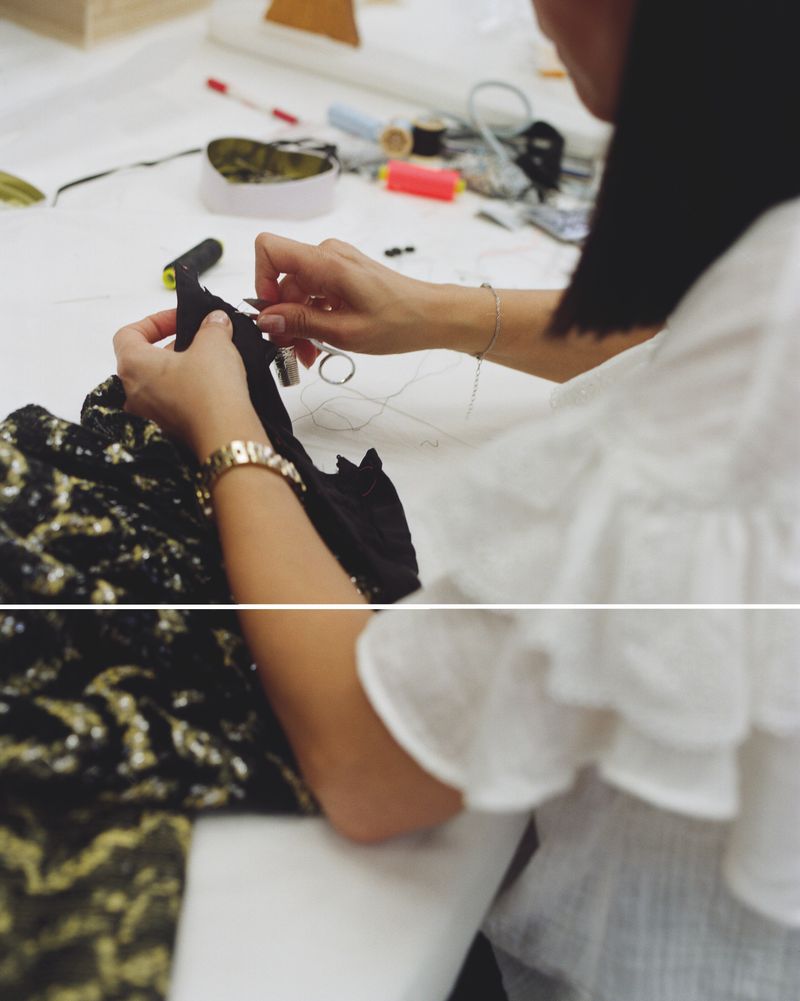 Woman sewing black and gold fabric with a needle and thread at a worktable. Close-up of hands, fabric, and sewing supplies on white.