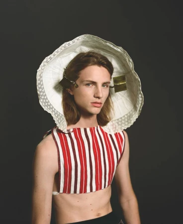 Unique fashion portrait of a young adult model wearing a lace bonnet and striped top against a dark gray backdrop in a studio.